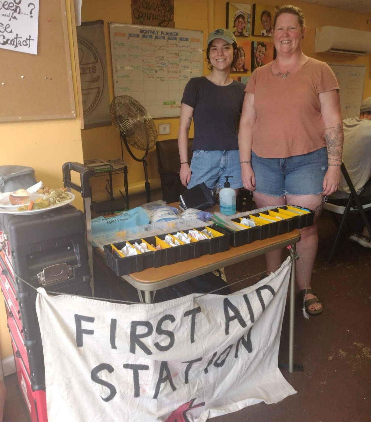 a pop-up tent, picnic tables and colorful signs outdoors. one sign reads "First Aid" and another reads "Se Habla Espanol"